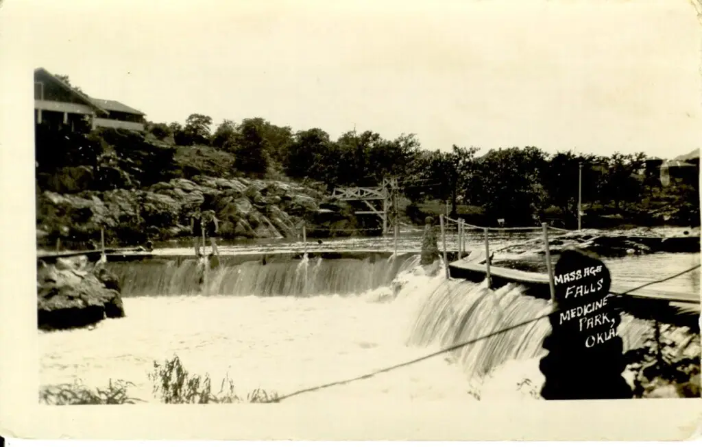 Historic black and white photo of Massage Falls in Medicine Park, Oklahoma, showing the waterfall, footbridge, and surrounding cobblestone landscape.